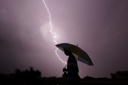 A pedestrian walks with an umbrella as lightning strikes during an evening thunderstorm in Jammu on May 14, 2015. AFP PHOTO / RAKESH BAKSHI (Photo by rakesh bakshi / AFP)