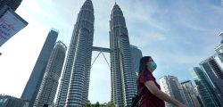 A woman wearing a face mask walks  in front of Twin Towers in Kuala Lumpur, Malaysia, Wednesday, March 18, 2020. For most people the new COVID-19 coronavirus causes only mild or moderate symptoms, but for some it can cause more severe illness. (AP Photo/Vincent Thian)