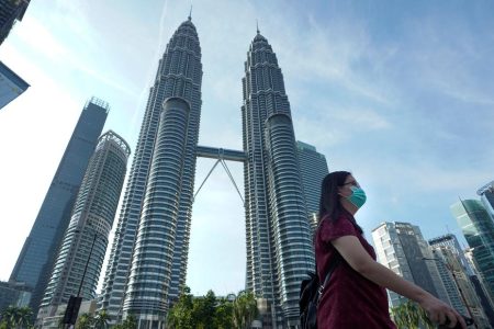 A woman wearing a face mask walks  in front of Twin Towers in Kuala Lumpur, Malaysia, Wednesday, March 18, 2020. For most people the new COVID-19 coronavirus causes only mild or moderate symptoms, but for some it can cause more severe illness. (AP Photo/Vincent Thian)