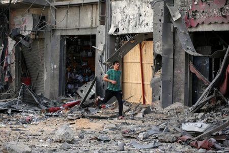 A Palestinian man runs for cover during an Israeli air strike near the site of a tower building which was destroyed in earlier strikes, amid a flare-up of Israeli-Palestinian violence, in Gaza City May 13, 2021. REUTERS/Suhaib Salem