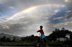 A-young-girl-plays-as-a-rainbow-is-seen-on-the-monsoon-sky-in-Kathmandu.