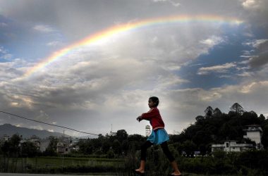 A-young-girl-plays-as-a-rainbow-is-seen-on-the-monsoon-sky-in-Kathmandu.