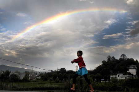A-young-girl-plays-as-a-rainbow-is-seen-on-the-monsoon-sky-in-Kathmandu.