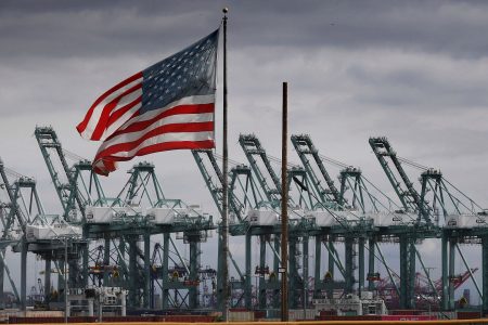 TOPSHOT - The US flag flies over shipping cranes and containers after a report said the United States and China are close to reaching a major trade deal that would see both sides lower some of the tariffs imposed during an often-bitter trade war, in Long Beach, California on March 4, 2019. (Photo by Mark RALSTON / AFP) (Photo by MARK RALSTON/AFP via Getty Images)