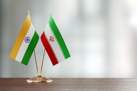 Indian and Iranian flag pair on desk over defocused background. Horizontal composition with copy space and selective focus.