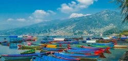 Many colourful boats parked on the shore of Phewa lake, Pokhara, Nepal. In the back Himalayan mountain range. Small villages visible on the shore. Peaceful and chilled atmosphere. Place to relax.