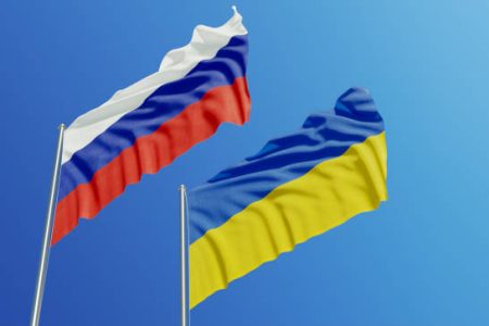 Russian and Ukrainian flags are waving with wind over  blue sky. Low angle view. Dispute and conflict concept. Horizontal composition with copy space.