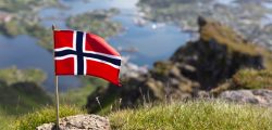 Norwegian Flag on the Nonstinden mountain. Blurred in the background the view down to Ballstad, Vestvågøya island, Lofoten Islands, Norway