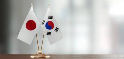 Japanese and South Korean flag pair on desk over defocused background. Horizontal composition with copy space and selective focus.
