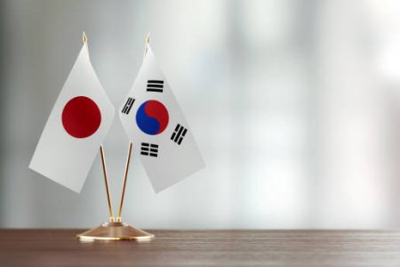 Japanese and South Korean flag pair on desk over defocused background. Horizontal composition with copy space and selective focus.