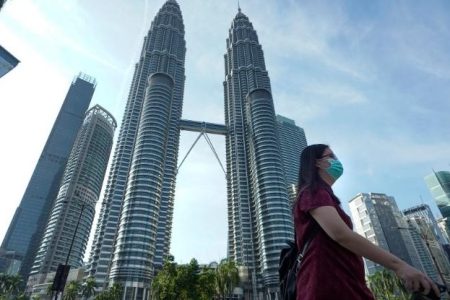 A woman wearing a face mask walks  in front of Twin Towers in Kuala Lumpur, Malaysia, Wednesday, March 18, 2020. For most people the new COVID-19 coronavirus causes only mild or moderate symptoms, but for some it can cause more severe illness. (AP Photo/Vincent Thian)