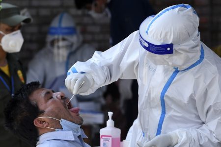 A health worker dressed in protective gear uses a swab to collect sample from a man for a coronavirus test at Kalimati vegetable market during a government-imposed nationwide lockdown as a preventive measure against the spread of the COVID-19 coronavirus, in Kathmandu on May 14, 2020. (Photo by PRAKASH MATHEMA / AFP)