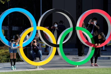 Visitors wearing protective face masks following an outbreak of the coronavirus disease (COVID-19) are seen through the Olympic rings in front of the Japan Olympics Museum, a day after the announcement of the games' postponement to 2021, in Tokyo, Japan March 25, 2020.  REUTERS/Naoki Ogura