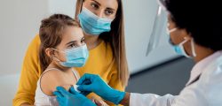 Female doctor placing adhesive bandage on little girl's arm after vaccination. Focus is on girl.