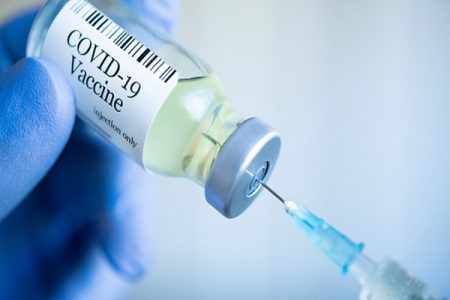 Doctor drawing up Covid-19 vaccine from glass phial bottle and filling syringe injection for vaccination. Close up of hand wearing protective disposable gloves in lab and holding a bottle of vaccination drugs. Hand with blue surgical gloves taking sars-coV-2 vaccine dose from vial with syringe: prevention and immunization concept.